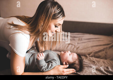 Mother holding crying baby lying in bed in room. Unhappy child. Looking at each other. Motherhood. Stock Photo