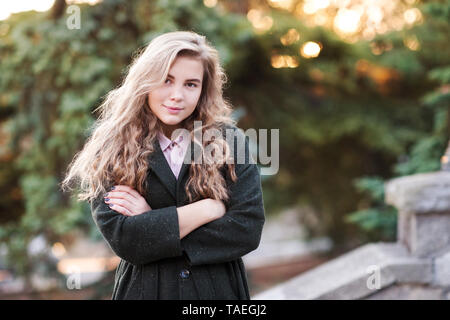 Stylish blonde teen girl 14-16 year old wearing stylish jacket outdoors over nature background closeup. Looking at camera. Teenagerhood. Fashionable. Stock Photo
