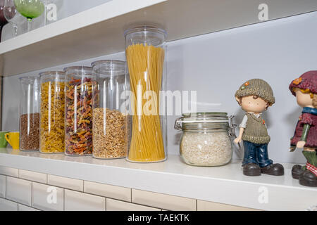 Various uncooked groceries in glass jars arranged on wooden white shelves ar the kitchen Stock Photo