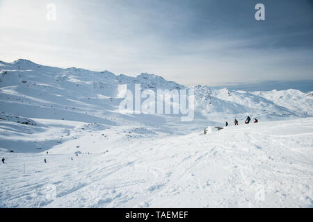 Panoramic landscape view with off piste skiers going down a slope in winter alpine mountain resort Stock Photo