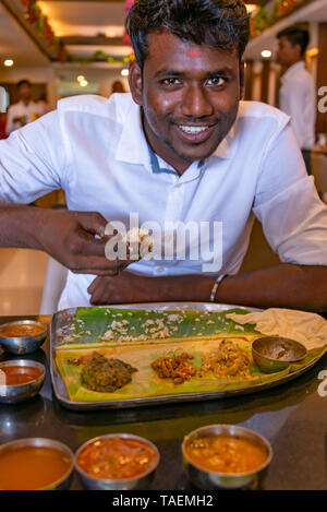 Vertical portrait of a man eating a typical vegetarian thali meal with his hands in India. Stock Photo