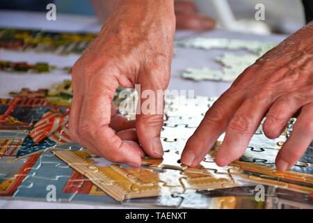 Older woman's hands working on puzzle for fun at family gathering in California USA America, real people, one missing fingers via accidental hobby Stock Photo