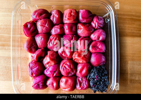 Traditional japanese storebought red umeboshi pickles made with ume plum flat top closeup on wooden table with pink shiso leaf Stock Photo
