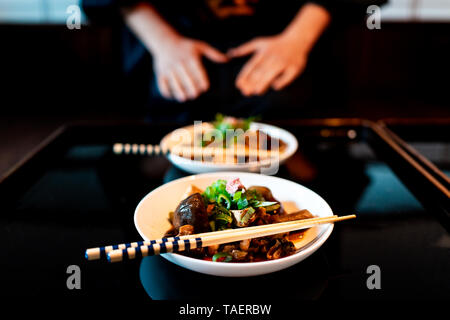 Traditional japanese machiya house or ryokan restaurant with black lacquered wood table and dish closeup with man in kimono or yukata background Stock Photo