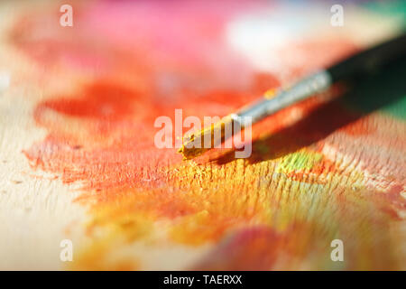 One brush, stained with yellow oil paint, lies on a wooden palette lit by the bright sun Stock Photo