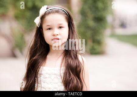 Beautiful kid girl 4-5 year old with long hair wearing bow headband outdoors close up. Looking at camera. Childhood. Stock Photo