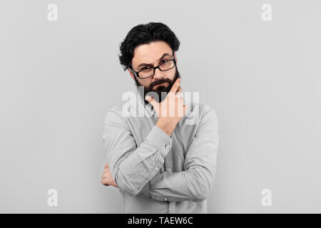 Thoughtful serious man wearing glasses, bearded thinking guy over gray background Stock Photo