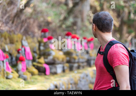 Nikko, Japan and young man looking at Jizo statues in famous Kanmangafuchi Abyss in Tochigi prefecture in Japan in early spring with moss Stock Photo