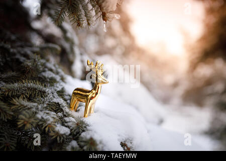 Golden toy deer stands on a branch of a Christmas tree in the snow in winter as a symbol of the New Year holiday Stock Photo