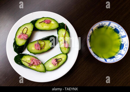 Japanese cucumber slices flat top on black wood table studio background and vegetable appetizer dish with salted pickled sakura flowers and green tea Stock Photo