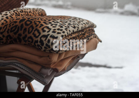 Closeup of a stack of multicolored blankets lying on a chair outside over a snowy landscape. Stock Photo