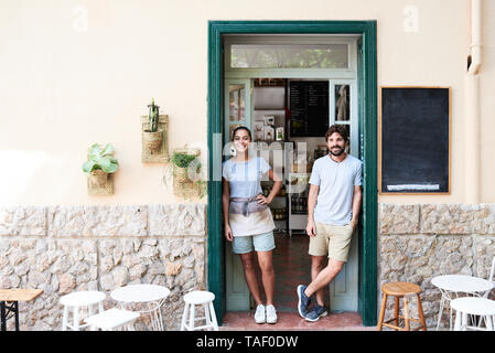 Portrait of smiling man and woman standing at entrance door of a cafe Stock Photo