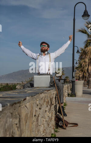 Happy man with laptop and longboard sitting on a wall Stock Photo