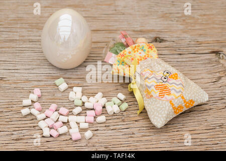On an old wooden background lies an embroidered little bag. The bag contains gifts, money and sweets. It is embroidered with a chick. Marshmallows and Stock Photo