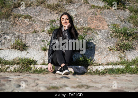 Portrait of smiling young woman sitting on curb Stock Photo
