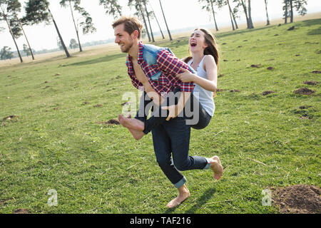 Happy young man carrying girlfriend piggyback on meadow Stock Photo