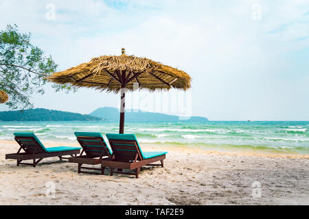 Two chaise longues under a straw umbrella on a beach near the sea. Tropical background. Coast of island Koh Rong Samloem, Cambodia. Stock Photo
