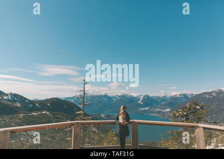 Mother holding her baby son on an observation deck, looking over Squamish, Canada Stock Photo