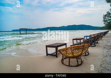 Wooden cafe table and chairs on a tropical beach with blue sea on background. island Koh Rong Samloem, Saracen Bay. Cambodia. Stock Photo