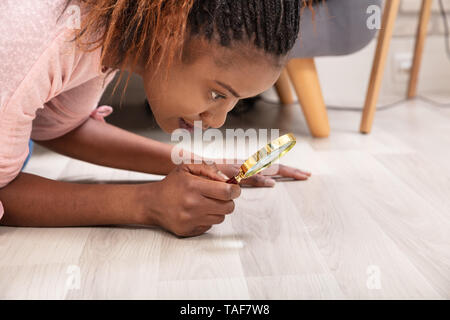 Side View Of A Young Woman Looking At Hardwood Floor Through Magnifying Glass Stock Photo