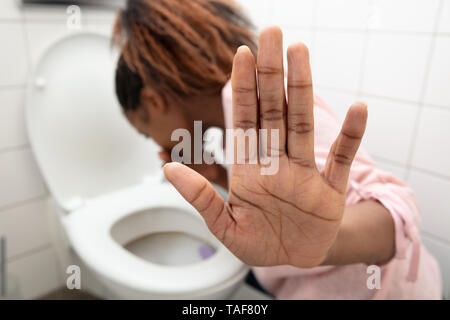 Close-up Of A Young Woman Showing Stop Sign While Vomiting In Toilet Bowl Stock Photo