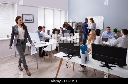 Confident Young Businesswoman Holding Document Walking In Front Of Her Colleagues In The Office Stock Photo