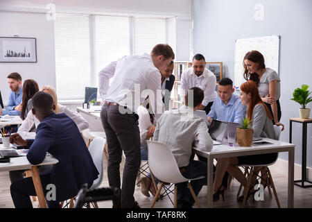 Group Of Young Diverse Business People Working And Communicating While Sitting At The Office Desk Stock Photo