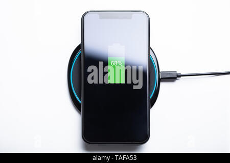 Smartphone Charging On A Wireless Charging Pad Over White Desk Stock Photo