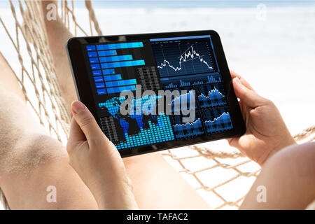 Close-up Of A Woman Lying On Hammock Analyzing The Graph On Digital Tablet At Beach Stock Photo