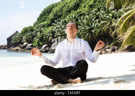 Portrait Of A Young Man In Formalwear Sitting On The Sandy Beach Mediating Stock Photo