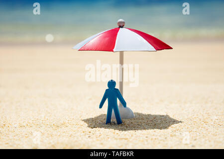 Close-up Of A Blue Human Figure Standing Under The Red And White Umbrella On Beach Stock Photo