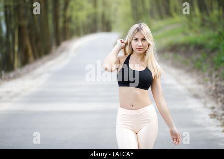 A young, sympathetic blond woman is actively spending time outdoors. The girl is dressed in sportswear. Stock Photo