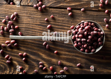 Raw, uncooked, dried adzuki (red mung) beans in metal spoon on rustic wood table background top view flat lay from above