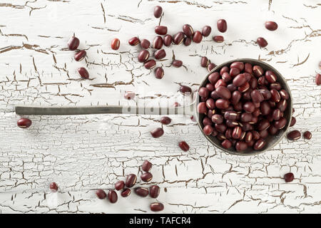 Raw, uncooked, dried adzuki (red mung) beans in metal spoon on white rustic wood table background top view flat lay from above Stock Photo