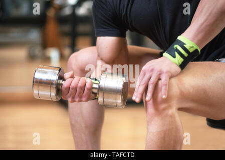 Handsome man doing biceps lifting with dumbbell on bench in a gym . Stock Photo