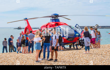 Lyme Regis, Dorset, UK. 25th May 2019. UK Weather: Crowds of holidaymakers and visitors flock to the beach at Lyme Regis to  bask in hot sunshine.  The Devon Air Ambulance helicopter generates interest amongst onlookers as it attends to an emergency on the busy beach. Credit: Celia McMahon/Alamy Live News. Credit: Celia McMahon/Alamy Live News Stock Photo