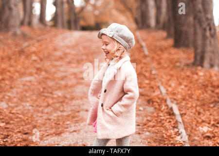 Smiling child girl 3-4 year old wearing trendy coat and knitted cap walking in park. Autumn season. Childhood. Stock Photo