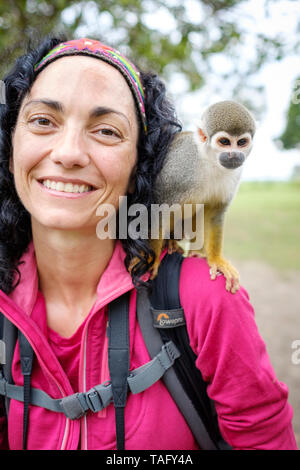 Tourist having a great time with a cute squirrel monkey on her shoulder at an animal shelter on the riverbank of the Amazon River near Iquitos, Peru Stock Photo