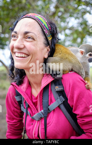 Tourist having a great time with a cute squirrel monkey on her shoulder at an animal shelter on the riverbank of the Amazon River near Iquitos, Peru Stock Photo