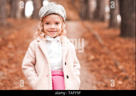 Smiling kid girl 3-4 year old wearing trendy winter jacket and cap outdoors. Walking in park. Autumn season. Childhood. Stock Photo