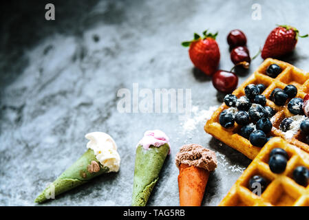 Sweet waffles with tasty red fruits full of healthy vitamins with some ice creams with waffle, over blue stone background with copy space for text. Stock Photo