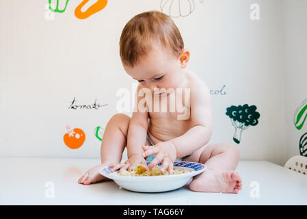 Baby eating by himself learning through the Baby-led Weaning method, exploring the flavors of food with curiosity. Stock Photo