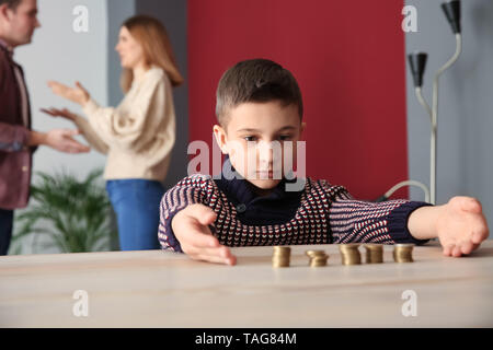 Sad little boy with coins and his quarreling parents at home. Concept of child support Stock Photo