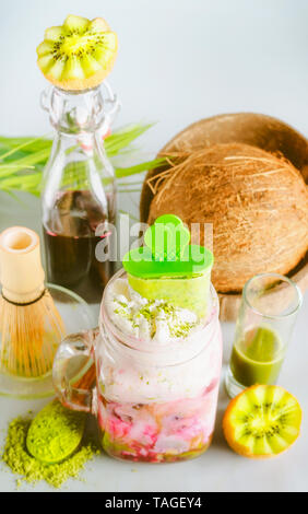 Vegan Matcha fusion drink with matcha ice cream in glass jar and ingredients: matcha espresso, red fruits juice, coconut milk. Healthy latte. Green te Stock Photo