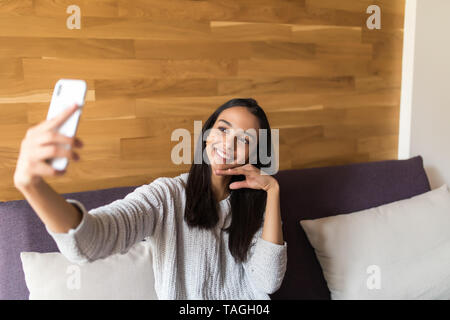 Portrait of a beautiful brunette taking a selfie with her smart phone at home Stock Photo