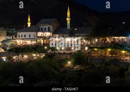 MOSTAR, BOSNIA AND HERZEGOVINA - AUGUST 13, 2015: Night photo of Tourist and locals in many restaurants over the Neretva river and mt. Hum in backgrou Stock Photo