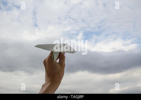 Human hand launching paper plane in cloudy sky Stock Photo