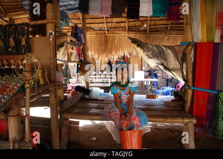 LONGNECK KAREN VILLAGE, THAILAND - DECEMBER 17. 2017: Young Long neck girl sitting lonely in a hut with thatched roof Stock Photo