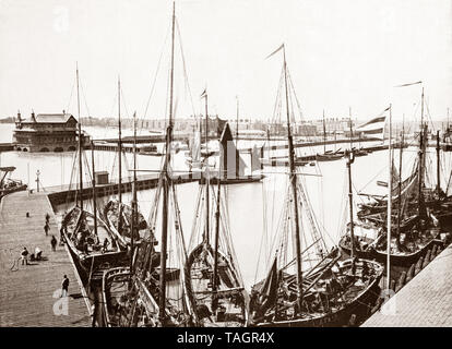 A late 19th Century view of fishing boats in Lowestoft harbour, an English town on the North Sea coast in the county of Suffolk. As a port town it developed out of the fishing industry and with wide, sandy beaches, two piers and other attractions it became a traditional seaside resort.  In the 19th century, the Lowestoft Railway & Harbour Company, connecting the town with Reedham and the city of Norwich, to help stimulate further development in the fishing industry. Stock Photo