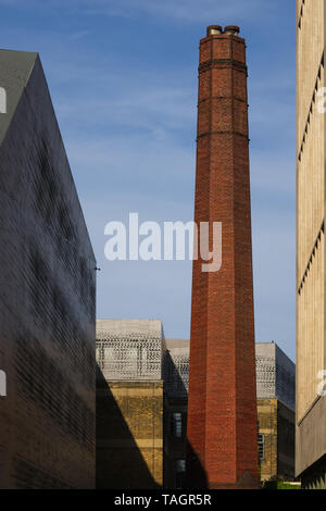 Long brown clay brick round chimney surrounded by brick wall buildings at dusk.